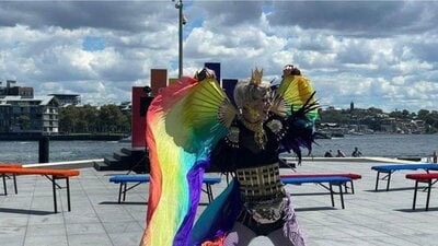 A drag king dances with rainbow fans and silks