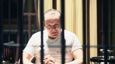 Older man sitting behind jail bars looking suspiciously at camera