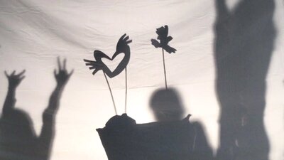 Shadow puppets move across a screen as the outlines of children dancing are visible on either side
