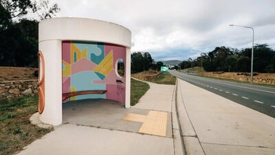 A picture of A Canberra Bus Stop with A painted internal artwork with blue yellow and pink