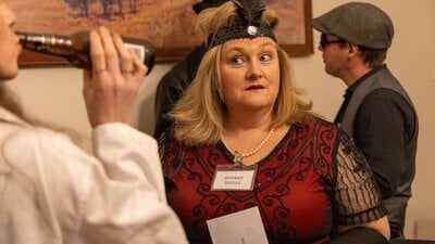 A woman in a red flapper dress considers new information as she attempts to solve the mystery