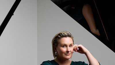 Emma Pask sits at a piano, looking nonchalant.