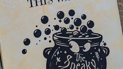 Sign pointing the way to The Sneaky Cauldron with a logo