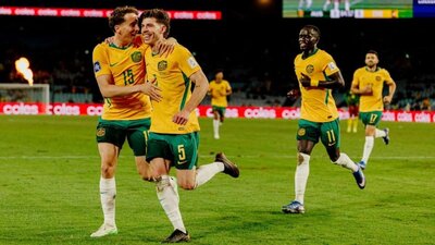 Soccer players in yellow kits celebrate a goal on a stadium pitch as teammates run in behind