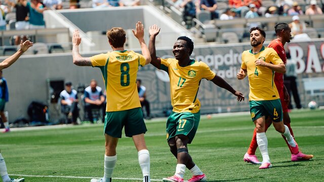 Soccer players in yellow kits celebrate a goal on a stadium pitch as teammates run in behind