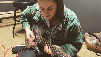 Young woman sitting on the floor jamming on guitar