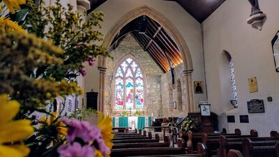 Flowers bloom inside an ancient stone and wood church with colourful stained glass