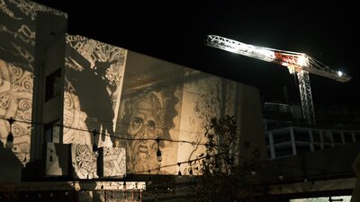 Space Cathedral Teaser Photo A projected artwork of a God-like figure staring at an illuminated construction crane.