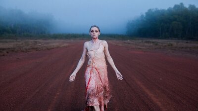 SPEAR (2015) woman drags her feet walking towards camera, in the desert covered in paint