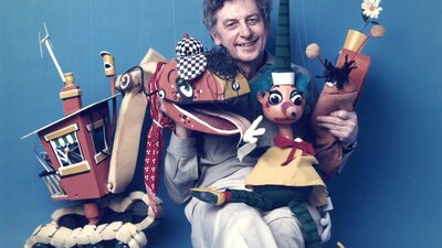 Photo of Norman Hetherington sitting down with his puppets and smiling at camera