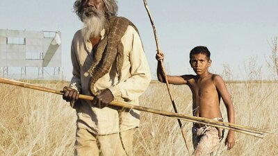 Older man and young boy walking through dry fields holding sticks