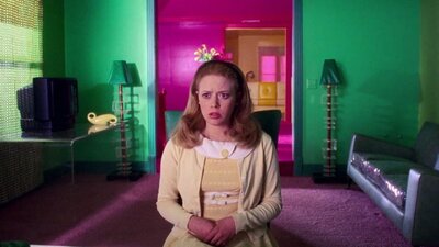 Woman sits in preppy outfit with her mouth open, pink door in background