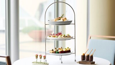 Three plates on high tea stand with two smaller dishes next to the stand.