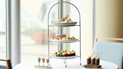Three plates on high tea stand with two smaller dishes next to the stand.