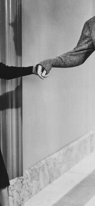 Black and white still of woman pulling a mans wrist to follow her