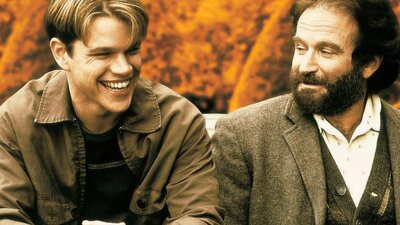 Two men sit next to each other, man on left laughing