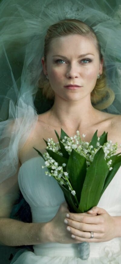 Woman with a blank expression lying down in white wedding gown and veil holding flowers