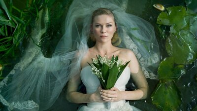 Woman with a blank expression lying down in white wedding gown and veil holding flowers