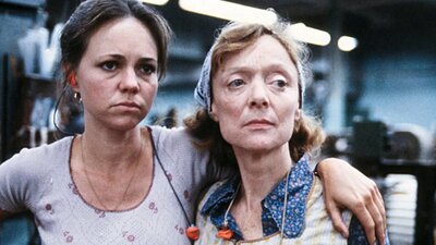 Two women look tired, one has arm over the other both looking to their left towards something