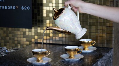 A photo of a teapot pouring a cocktail into a teacup at a bar.
