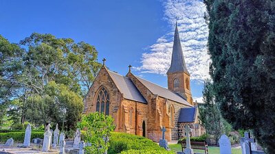 An old sandstone church with a graveyard in the foreground interspersed with green trees and plants
