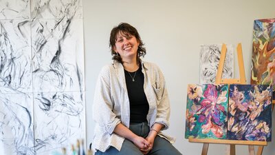 Sarah Murray sitting beside her artworks in her studio.