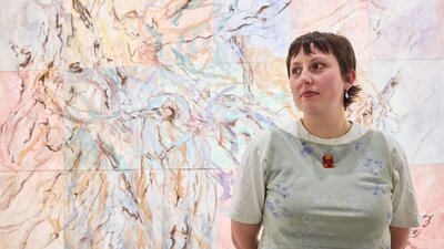 The artist, Sarah Murray, stands in front of an abstract painting.