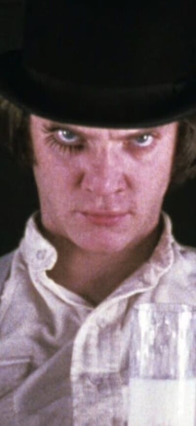 A Clockwork Orange (35mm) – Sat 8 Nov, 7:00 PM Man wearing hat and make up on right eye glares at camera holding glass of milk