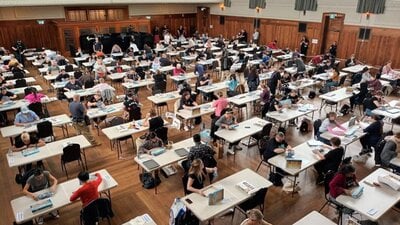 A large room with lots of people sitting at tables completing puzzles