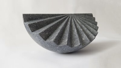Origami by Senden Blackwood A sculpture of dark stone in a semi-cicle with ridged relief like a hand fan.