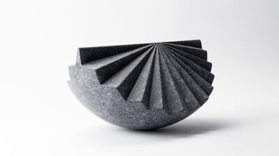 Origami by Senden Blackwood A sculpture of dark stone, of a segment of a sphere with contours like a fan.