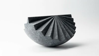 A sculpture of dark stone, of a segment of a sphere with contours like a fan.
