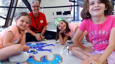 Children sitting with a museum host with a mosaic artwork