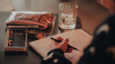 Person sketching with pastels and pencil case next to them