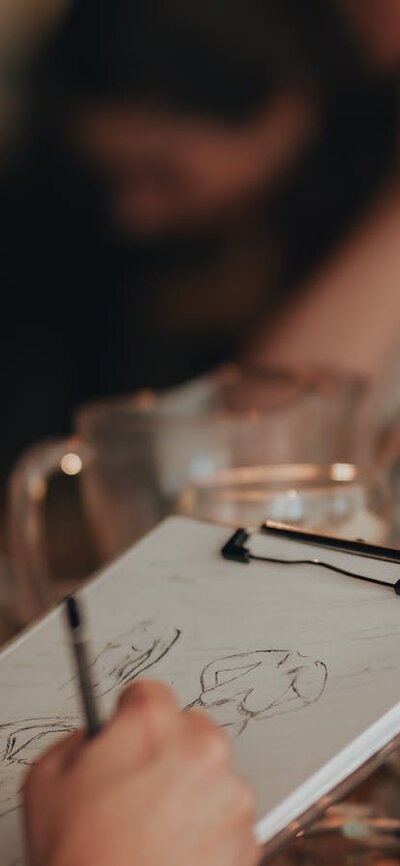 Person drawing in foreground, with glasses of beer on table