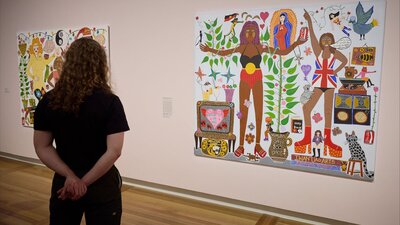 Visitor looking at Anangu Kungka & London Lady 2020 © Iwantja Arts A woman looks at a colourful, eclectic portrait by Kaylene Whiskey that hangs on a pale pink wall.