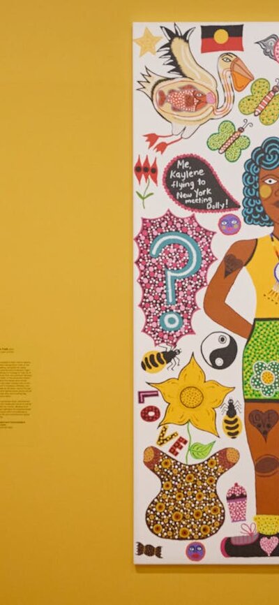 Two young people view a portrait, and in the foreground, a colourful portrait hangs on a yellow wall