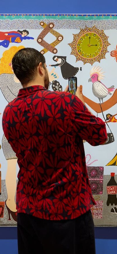 A person in a floral shirt takes a photo of a colourful portrait of Kaylene Whiskey and Dolly Parton