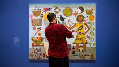 A person in a floral shirt takes a photo of a colourful portrait of Kaylene Whiskey and Dolly Parton