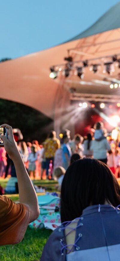 People sitting on grass, looking up at stage as they watch outdoor performance