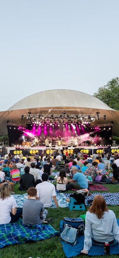 People sitting on grass, looking up at stage as they watch outdoor performance