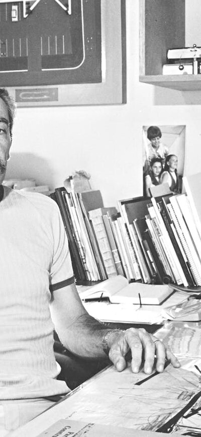 Enrico Taglietti in studio, 1985, photo by Ted Richards Enrico Taglietti holding a pen at his desk in his studio, photo taken in 1985