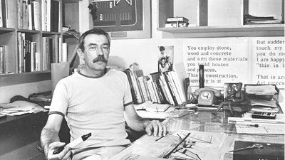 Enrico Taglietti holding a pen at his desk in his studio, photo taken in 1985