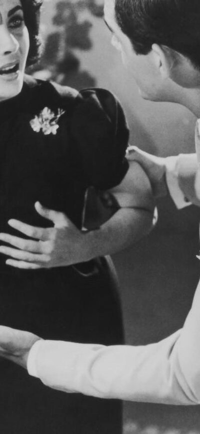black and white still of woman looking distressed and man speaking to her