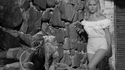Black and white image of woman squinting at camera in white top with an Iguana to her left