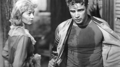 A Streetcar Named Desire in 35mm (1951) Black and white image of man taking off his jacket walking past woman staring at him