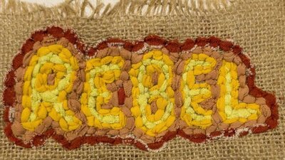 Henry Shawcross | Textile Works 2025 The word "Rebel" in yellow and red, made using the rag rugging technique