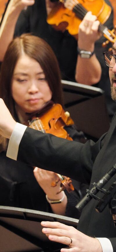 Louis Sharpe conducting CCS & NCO Missa Solemnis concert, Llewellyn Hall 6 July 2024 Louis Sharpe conducting with violin players around him.