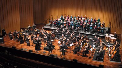 Soprano, tenor and bass soloists, conductor, orchestra and choir performing on stage.