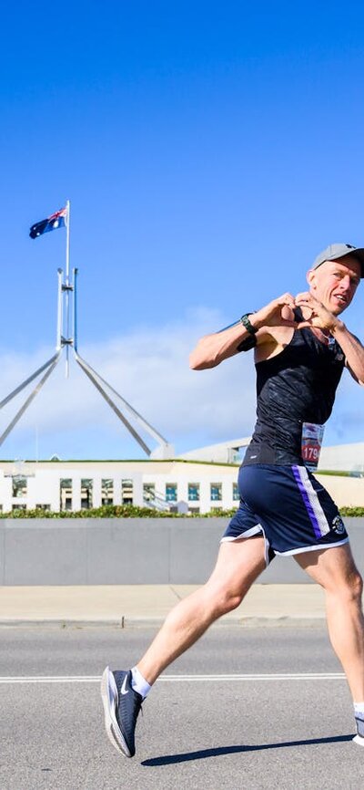 Man running past the Parliament House while doing the heart sign with his hands.